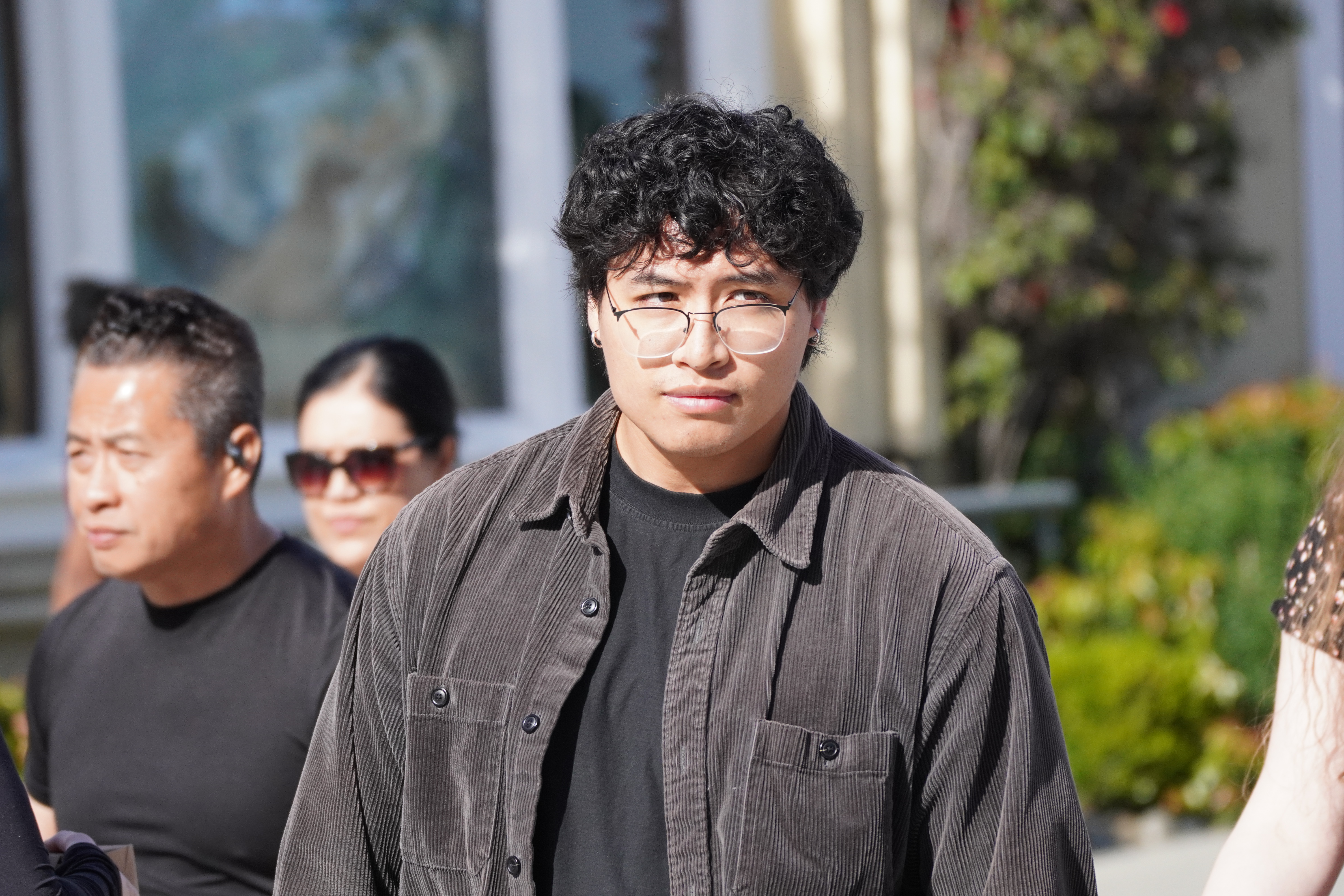 Portrait of a person with curly hair and glasses walking outdoors in sunlight